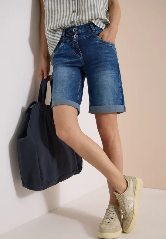 Personne porte un short en jean jusqu'au genou, un top rayé, des baskets et un sac bleu foncé.