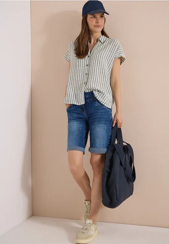 Personne en chemise à rayures, bermudas en jean, baskets, casquette et grand sac bleu.