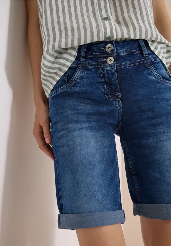 Femme en haut rayé et short en jean retroussé devant un mur blanc