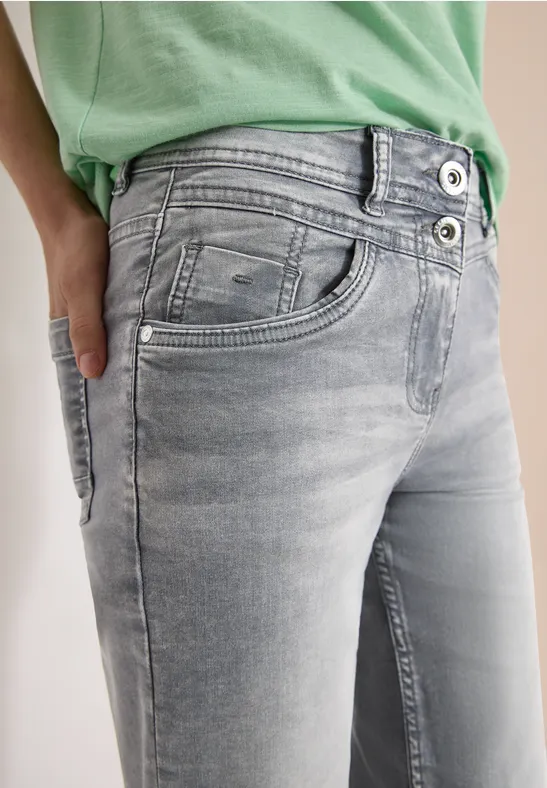 Nahaufnahme einer Person in hellgrauen Jeans und grünem Shirt mit Hand in der Hosentasche.