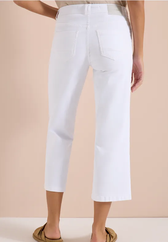 Vue de dos d’une personne portant un jean blanc large et court au-dessus des chevilles sur fond beige.