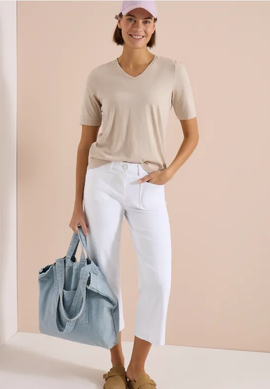 Femme en t-shirt beige, pantacourt blanc et grand sac cabas bleu clair sur fond neutre.
