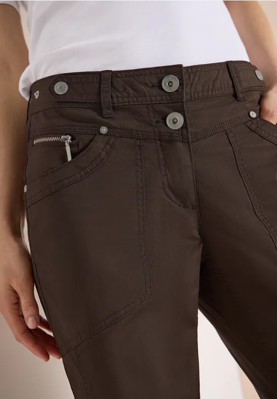 Braune Hose mit seitlicher Reißverschlusstasche, zwei Knöpfen und dekorativen Nahtdetails.