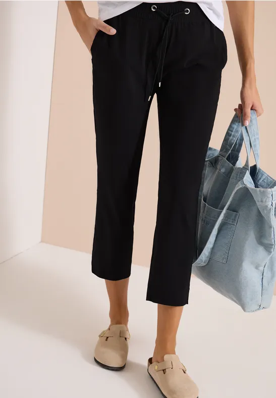 Schlanke, knöchellange schwarze Hose mit Tunnelzug, beigefarbene Schuhe und große Jeans-Tasche.