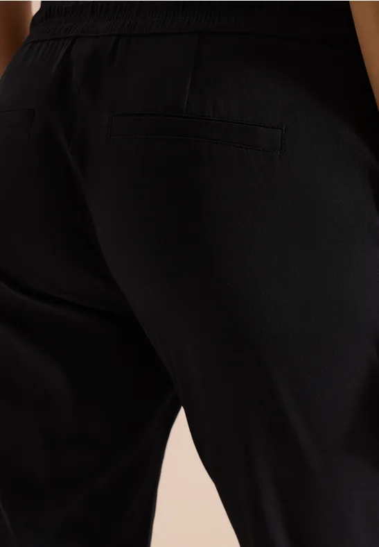 Nahaufnahme einer Person in schwarzen Hosen, seitliche Gesäß- und Beinpartie mit Eingrifftasche.