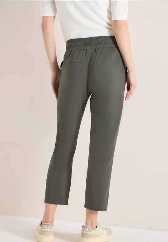 Vue arrière d'une personne portant un pantalon kaki court à taille élastique, un haut blanc et des baskets beiges.