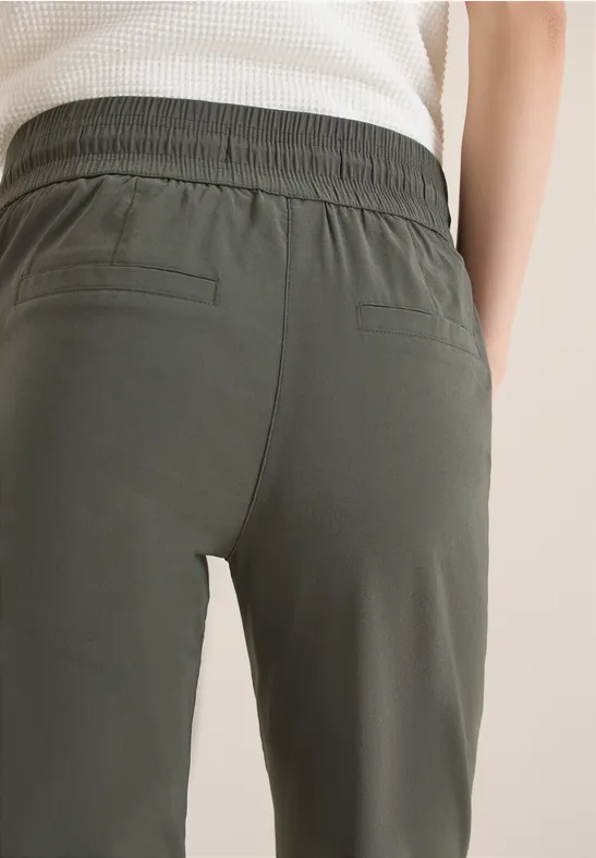 Gros plan d'une personne de dos portant un pantalon olive à taille élastique et deux poches arrière.