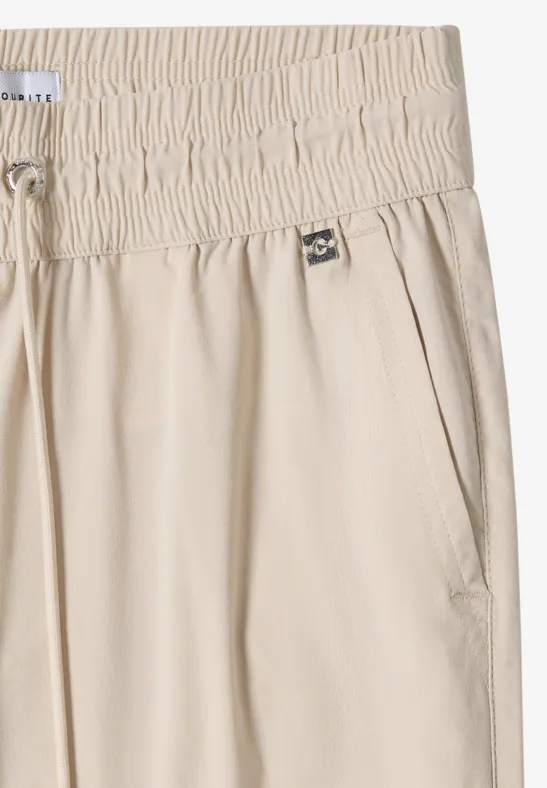 Beige Hose mit hohem, gerafftem Elastikbund, Kordelzug und seitlichen Eingrifftaschen.