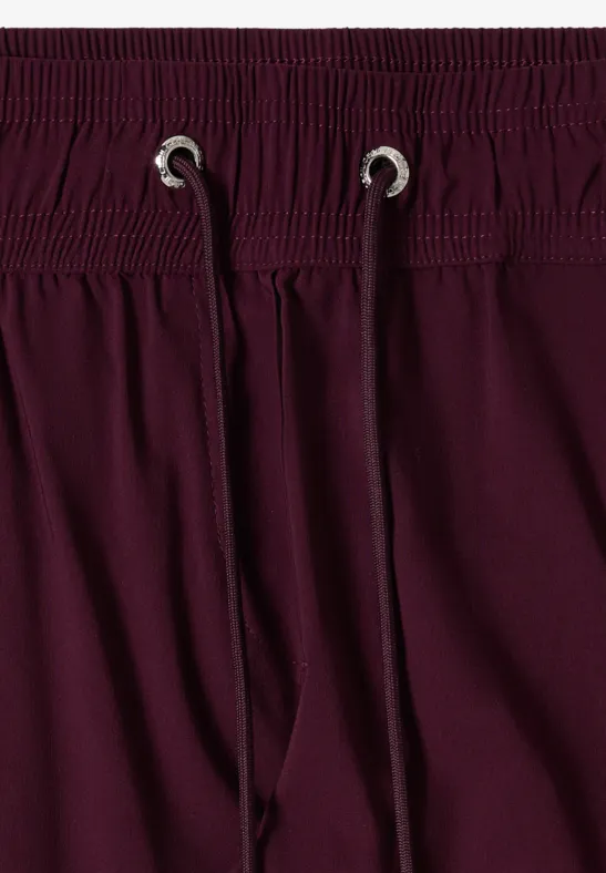 Nahaufnahme einer dunkellila Hose mit elastischem Tunnelzugbund und silbernen Ösen.