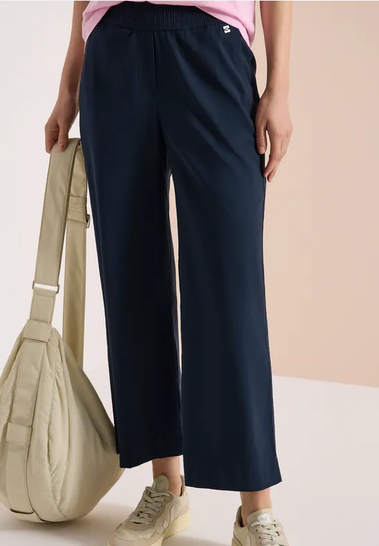 Weite marineblaue Damenhose mit Gummibund, grüne Sneaker und große beige Tasche