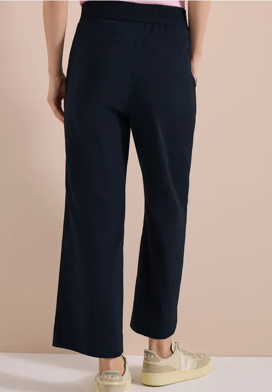 Frau von hinten in dunkelblauer, weit geschnittener Hose mit elastischem Bund und beigen Sneakern.