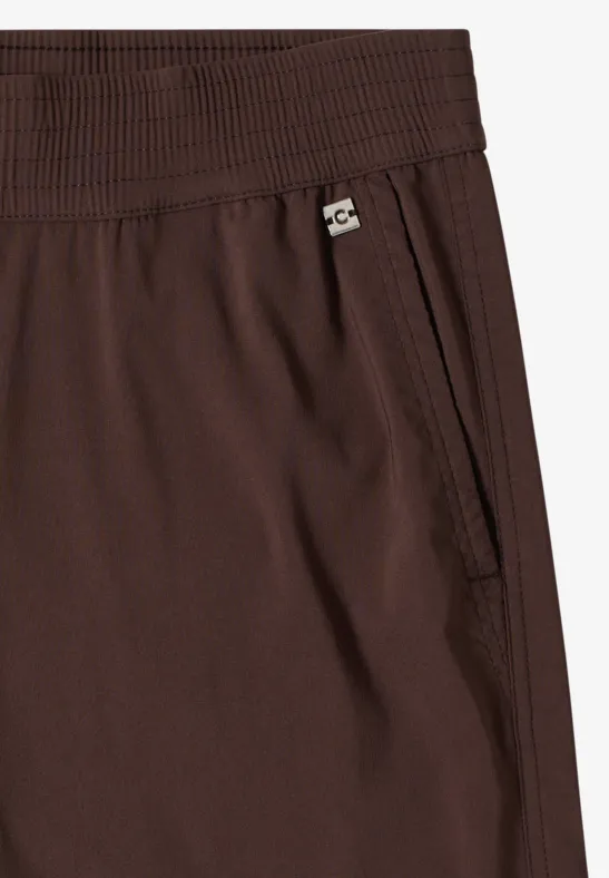 Braune Hose mit elastischem Bund, seitlicher Tasche mit Reißverschluss und kleinem Logo-Label.
