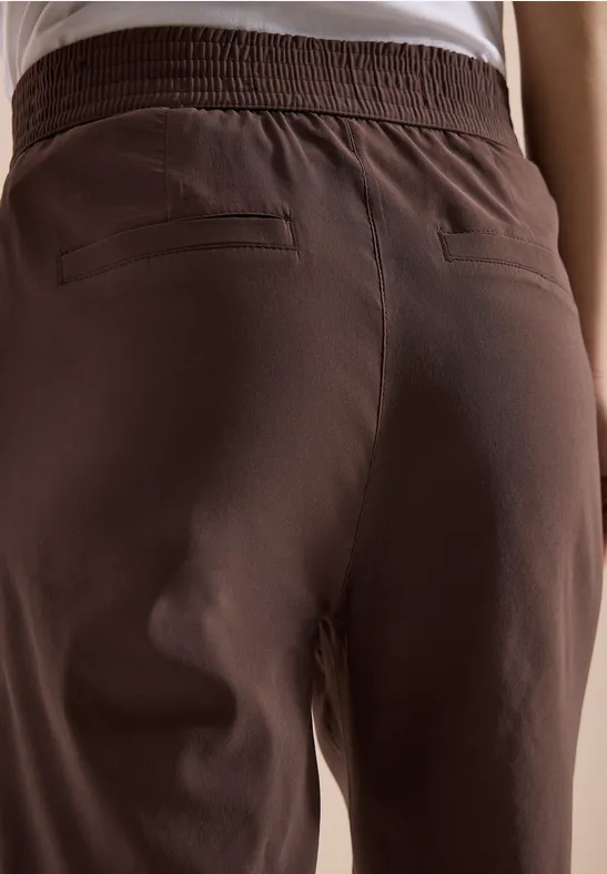 Hinteransicht einer Person mit brauner Hose und weißem Oberteil.