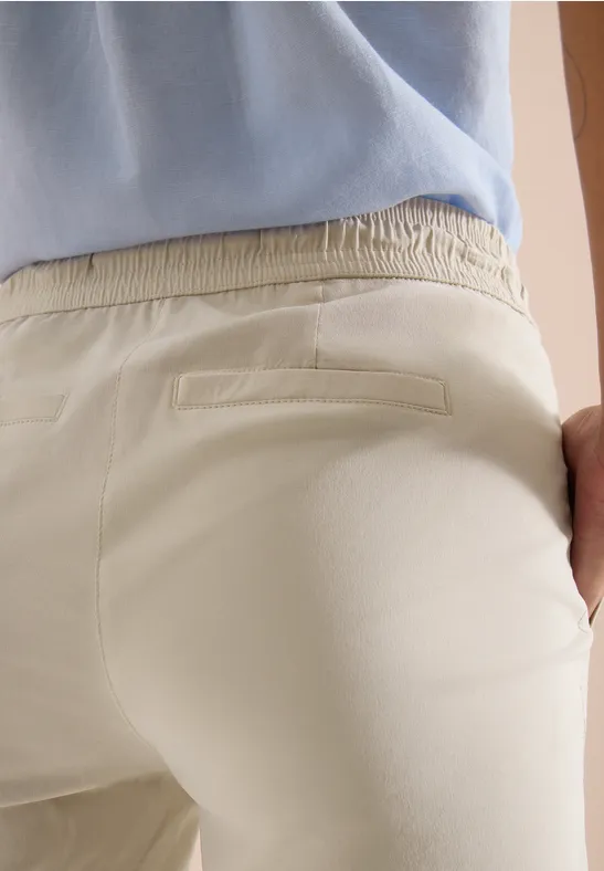 Eine Person von hinten in hellbeigen Hosen und blauem Oberteil, die rechte Hand in der Gesäßtasche.