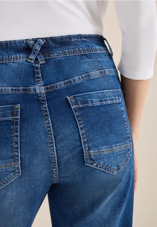 Rückenansicht einer Person in blauer Jeans mit Gesäßtaschen und weißem Oberteil.