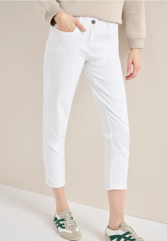 Weißer, knöchellanger Damen-Jeans mit schmalem Schnitt und Seitentasche, kombiniert mit grünen Sneakern.