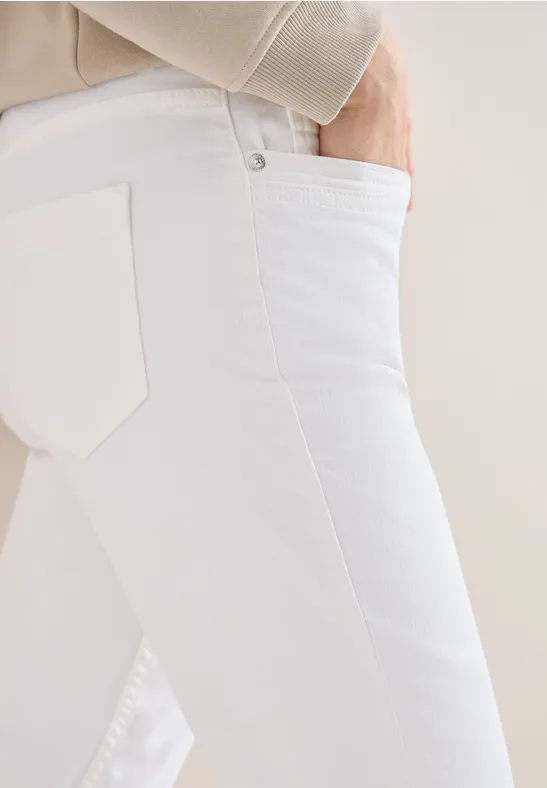 Nahaufnahme einer Person in weißen Jeans mit Hand in der vorderen Hosentasche vor neutralem Hintergrund.