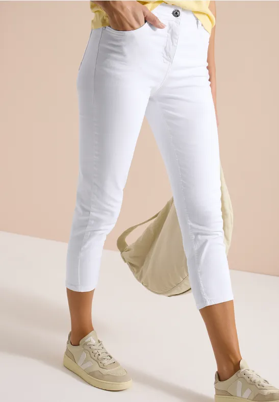 Frau trägt weiße 7/8-Jeans, helle Sneaker und eine beige Tasche.