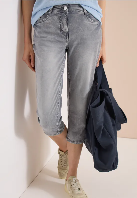 Graue Capri-Jeans, leger hochgekrempelt, weiße Sneaker, dazu blaue Tasche.