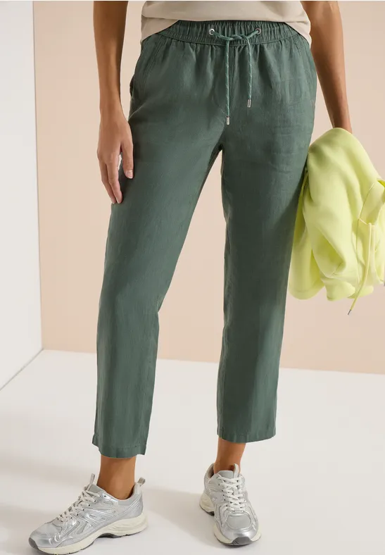 Personne porte un pantalon vert à cordon de serrage, baskets argentées, tient une veste néon.