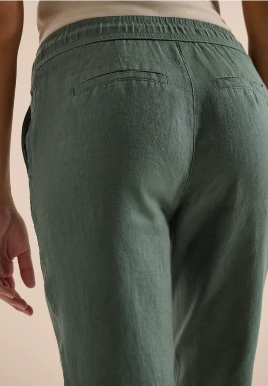 Gros plan sur une femme en pantalon vert en lin, vue de la taille et des hanches.