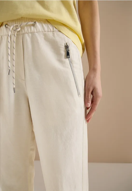 Beige Freizeithose mit Reißverschlusstasche und Kordelzug, dazu ein gelbes Shirt.