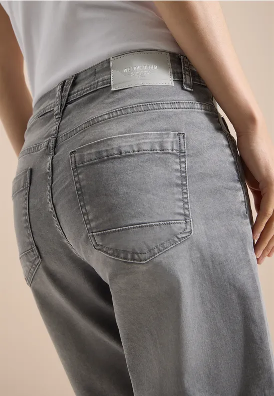 Person in grauen Jeans und weißem Top von hinten, Fokus auf Gesäßbereich.