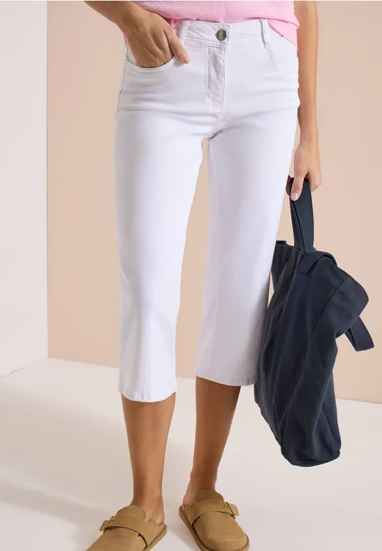 Weiße Capri-Jeans kombiniert mit einem pastellfarbenen Top, legeren Loafers und einer dunkelblauen Jacke.