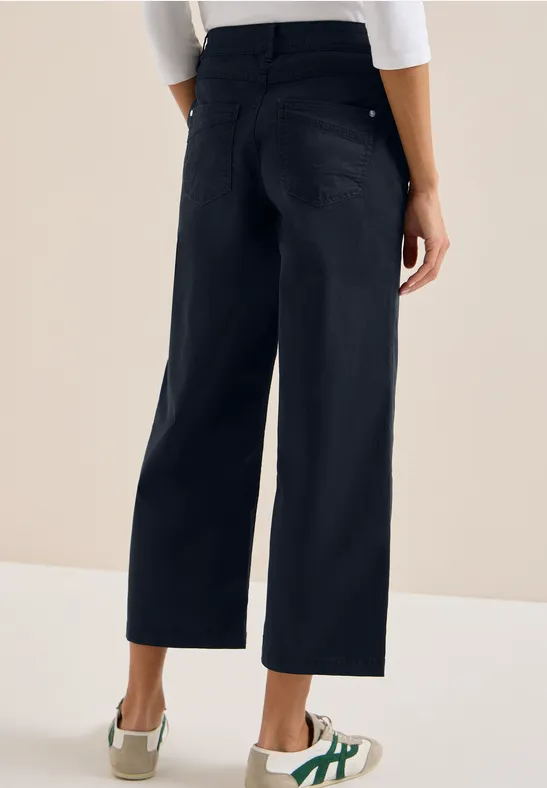 Schlanke schwarze Culotte-Hose, hinten mit Taschen, kombiniert mit weißen Sneakern