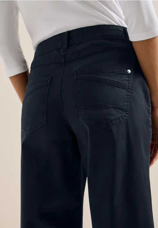 Person von hinten in dunkelblauer, taillierter Hose und weißem Oberteil.