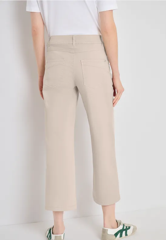 Beige 7/8-Hose mit weitem Bein und Gesäßtaschen, locker geschnitten, kombiniert mit weißem T-Shirt vor hellem Hintergrund