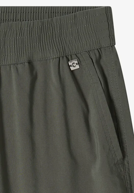 Olivgrüne Hose mit elastischem Bund, seitlicher Tasche und kleinem Metall-Logo in Nahaufnahme.