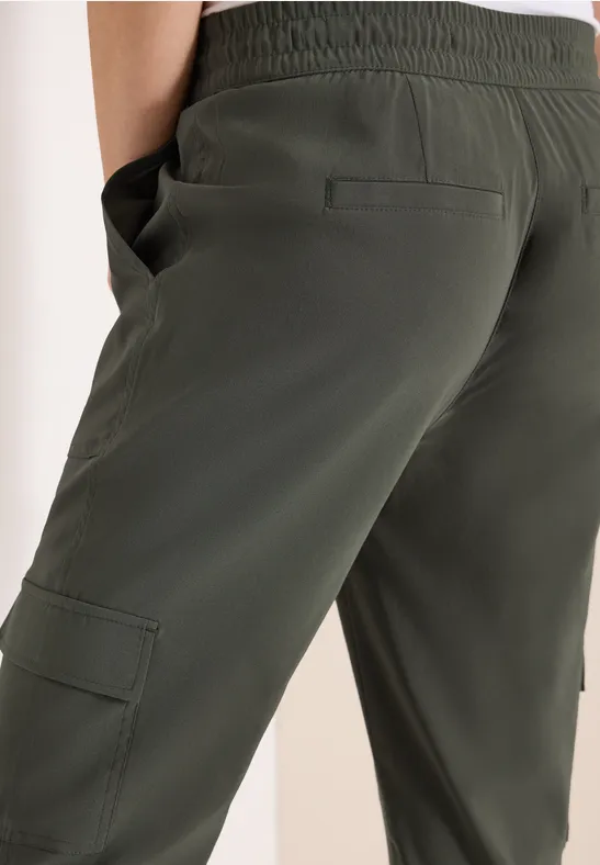Dunkelgrüne Cargo-Hose mit elastischem Bund, Seitentaschen und Cargotasche am Oberschenkel.