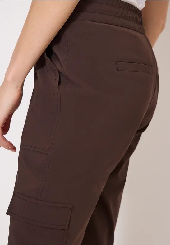 Seitliche Ansicht einer Person in brauner Cargo-Hose mit elastischem Bund und aufgesetzten Taschen.