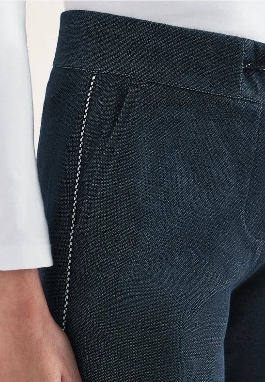 Nahaufnahme einer dunkelblauen Hose mit seitlicher Zierpaspel und weißem Oberteil.