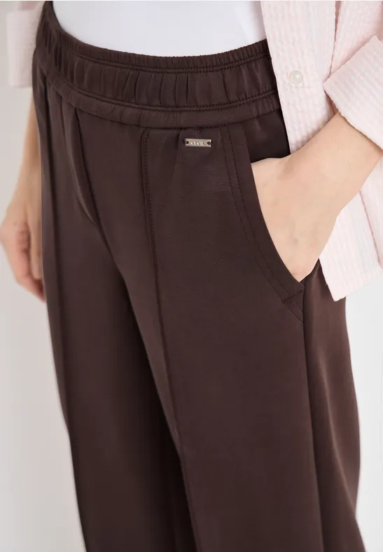Braune Freizeithose mit Gummibund und seitlichen Eingrifftaschen, Hand in Tasche.