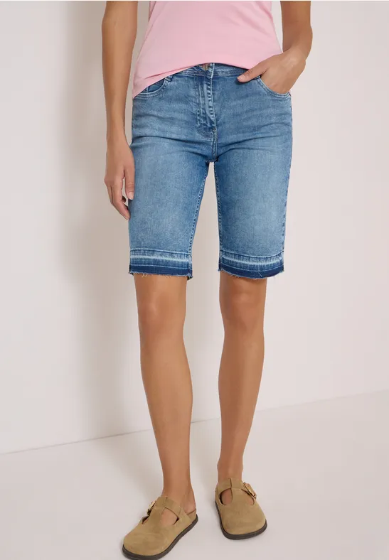 Femme porte un short en jean bleu clair jusqu'aux genoux et des sandales marron, haut rose visible.