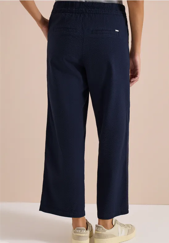 Rückenansicht einer Person in marineblauer, weiter, knöchellanger Hose und hellen Sneakern.