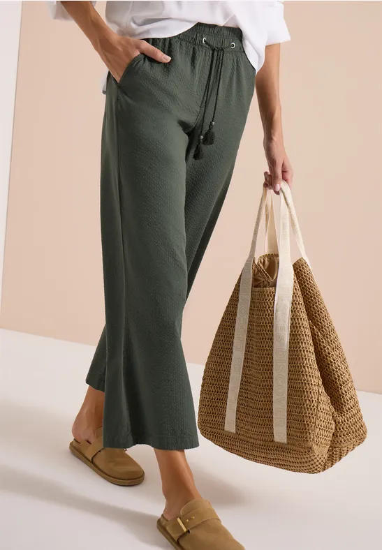 Dame mit weiten grünen Hosen, weißem Oberteil und großer Basttasche