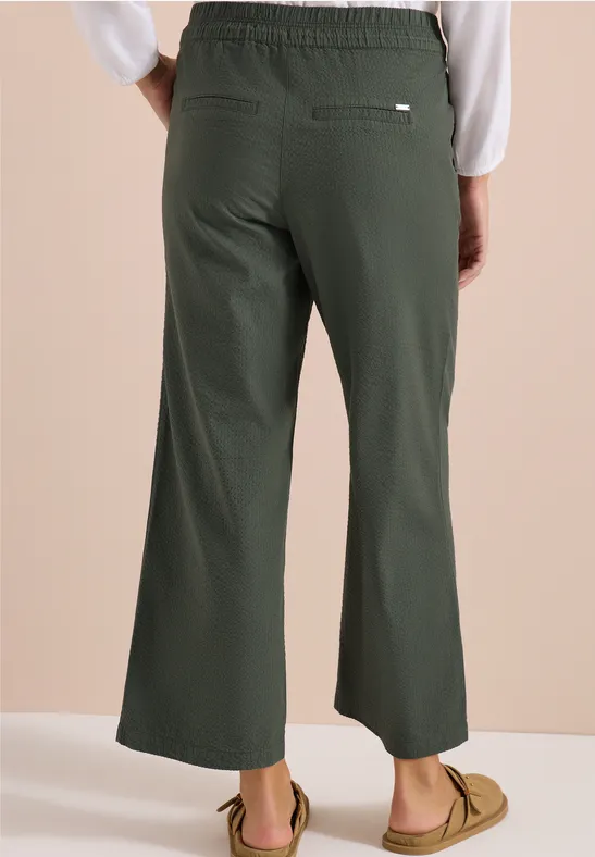 Rückenansicht: Modell trägt dunkelgrüne, weite, knöchellange Hose mit Gummibund und lässigen Mokassins.