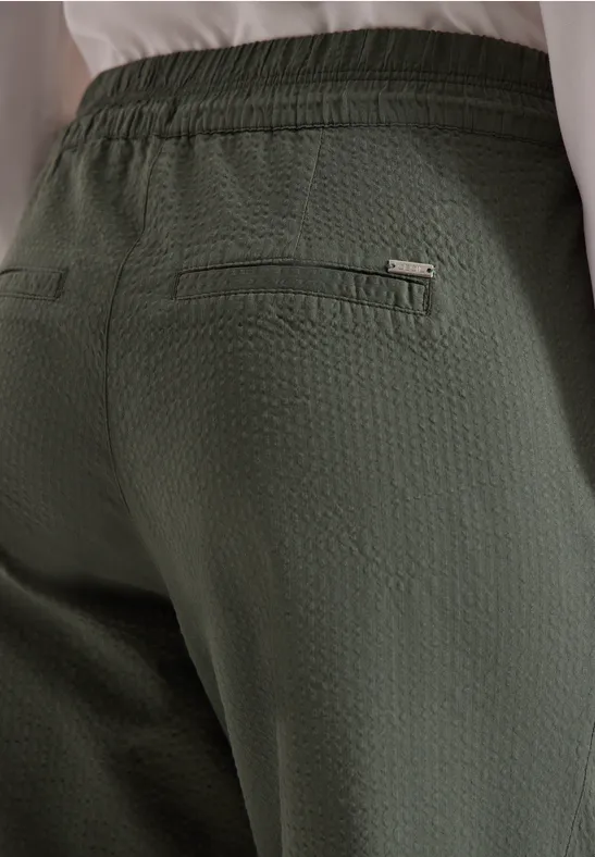 Rückansicht einer Person in olivgrüner, strukturierter Hose mit Reißverschlusstasche.