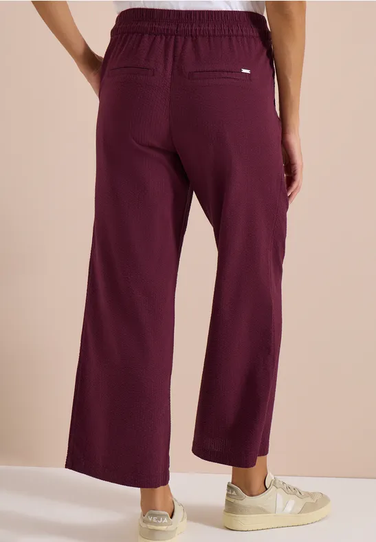 Modell trägt weite, dunkelrote Hose mit Gummibund, Rückansicht.