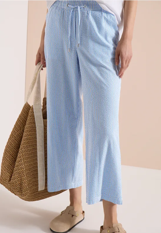 Locker sitzende hellblaue Culotte, braune Sandalen und große Strohtasche