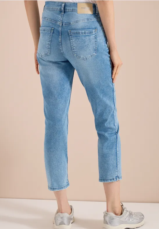 Frau trägt hellblaue, knöchellange Jeans mit geradem Schnitt und grauen Turnschuhen.