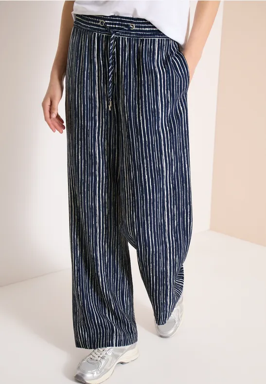 Weit geschnittene, dunkelblaue Hose mit weißen Streifen, Tunnelzugbund und Taschen, kombiniert mit weißen Sneakern.