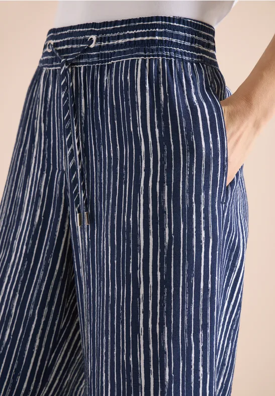 Lockere blaue Hose mit weißen Längsstreifen, elastischem Bund und seitlichen Taschen.