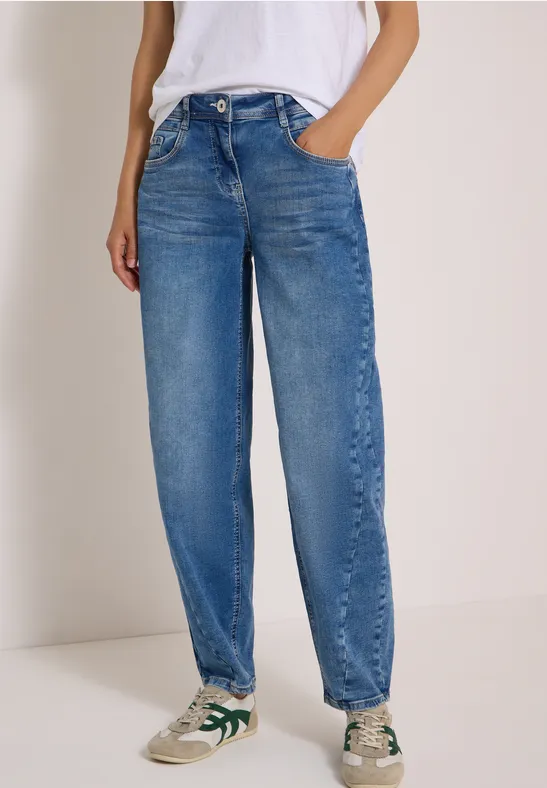 Person trägt lockere, hoch taillierte blaue Jeans und weiße Sneaker mit grünen Akzenten.