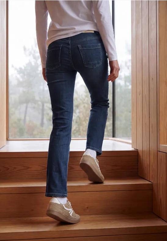 Jambes en jean et baskets montant un escalier en bois devant une fenêtre.