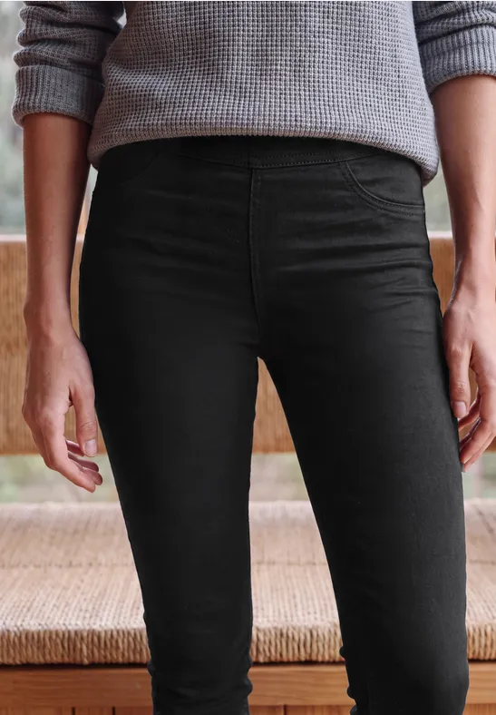 Une personne porte un pantalon noir moulant et un pull gris, cadrés de la taille aux genoux.
