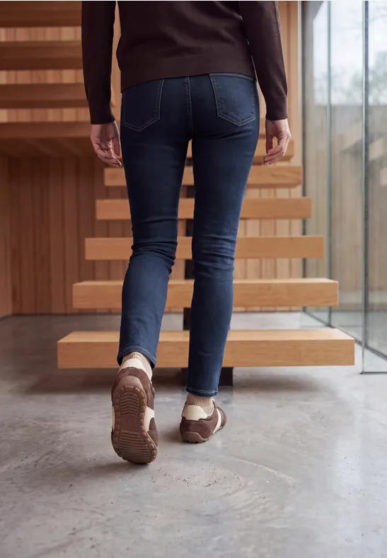 Une personne en jean et chaussures marron monte un escalier moderne.